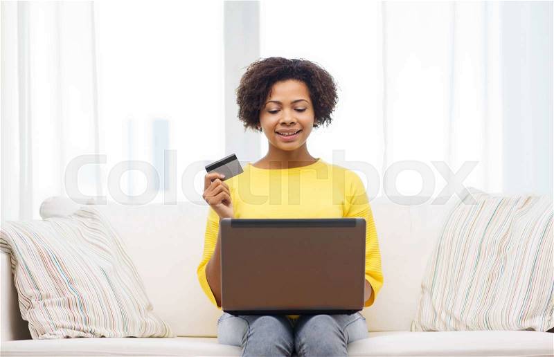 People, internet bank, online shopping, technology and e-money concept - happy african american young woman sitting on sofa with laptop computer and credit card at home, stock photo