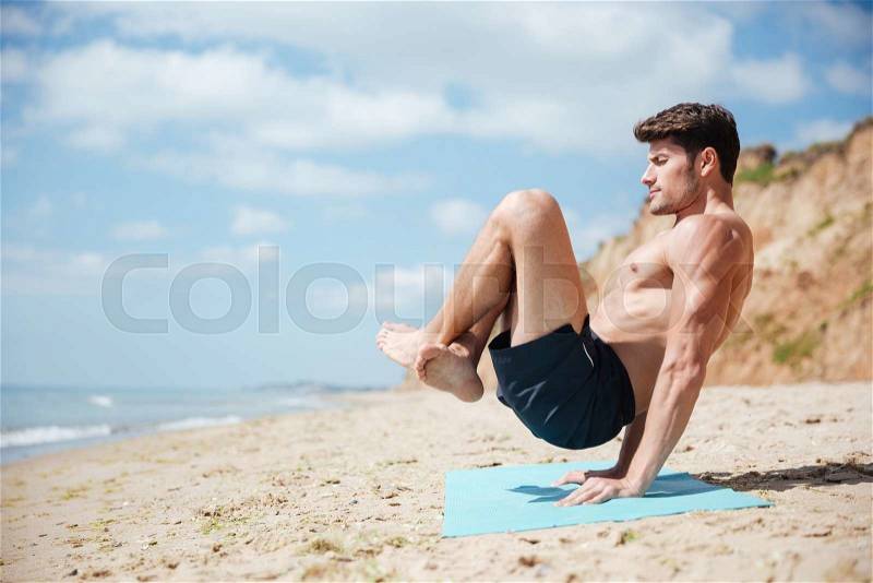 Man with eyes closed balancing on his hands and practicing yoga on the beach, stock photo