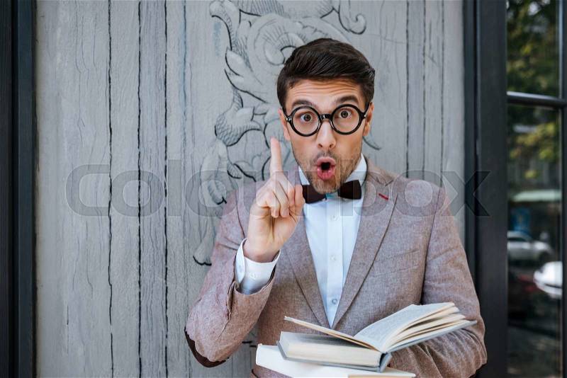 Young stylish nerd man with books got an idea outdoors, stock photo