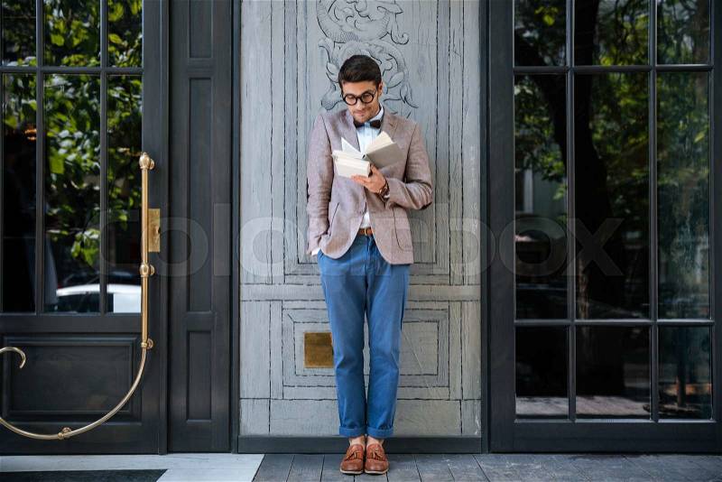 Young stylish nerd man reading books outdoors, stock photo