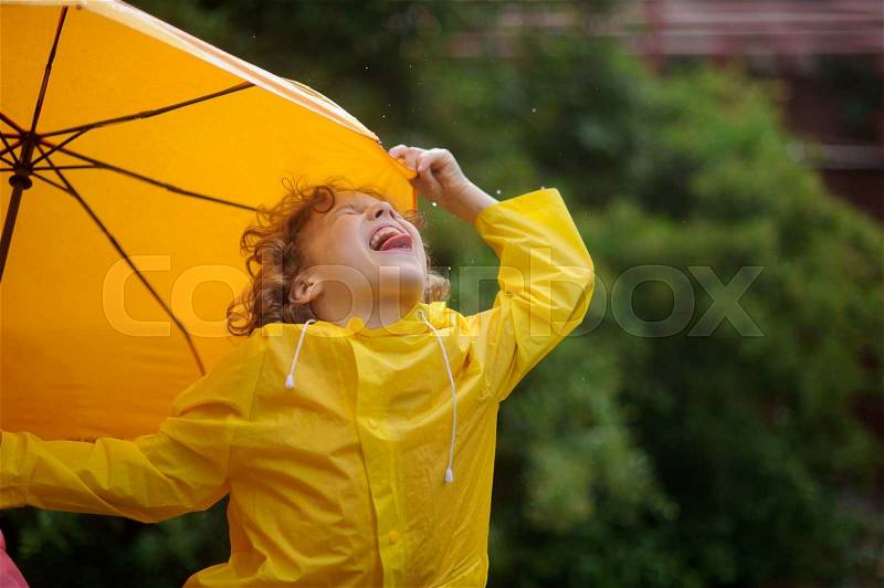 The little boy tongue catches rain drops. He has thrown back the head and has closed eyes. A hand holds an umbrella, stock photo