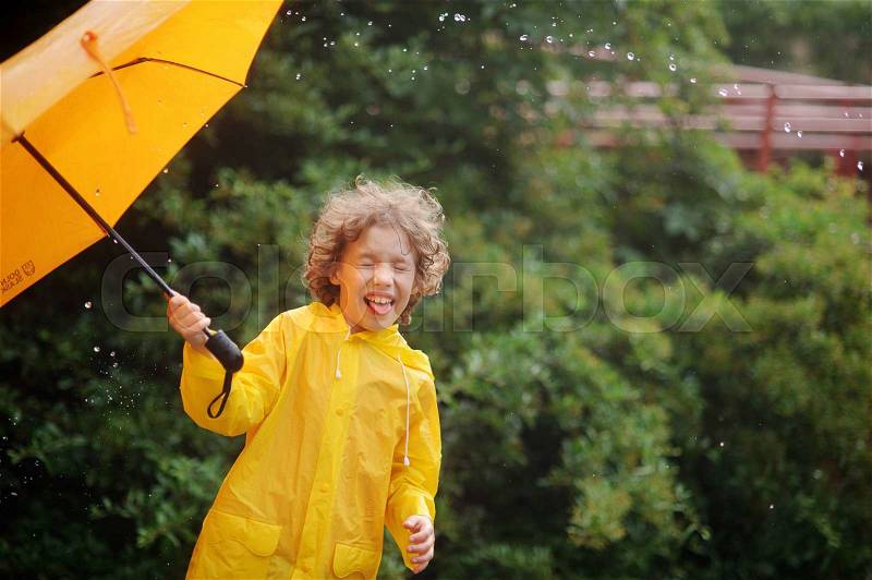 Boy of 8-9 years with an umbrella in a hand to stand in the rain. Large drops of a rain fall to it on the head. Little fellow closed eyes from delight.Behind the back there is a magnificent green bush, stock photo