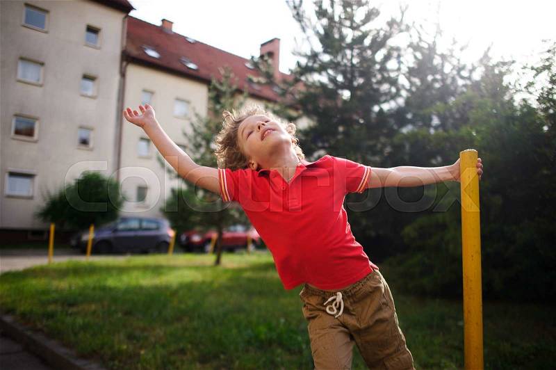 The little boy of 8-9 years turns around a support in the yard of the house. He imagines something during game. The boy has thrown back the head and has closed eyes from delight, stock photo