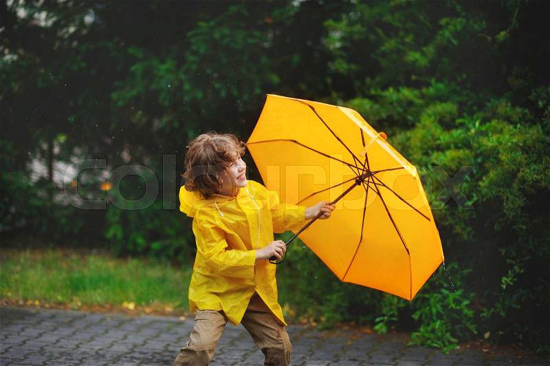 8-9 years boy walking in the rain. The little fellow in a yellow raincoat with a yellow umbrella walks in park under a small summer rain. On his face a smile. Walk it gives pleasure, stock photo