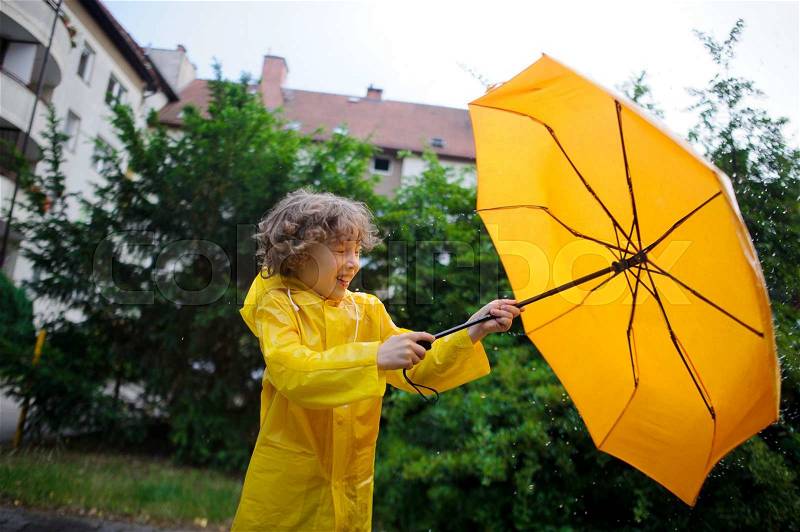 Boy is closed by a big yellow umbrella from a rain and wind. He hardly holds an umbrella. Chappie has closed eyes, stock photo
