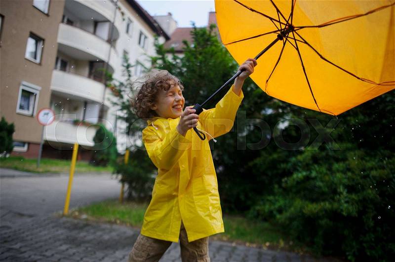 Cheery lad walks in the rain in the yard of the house with a yellow umbrella. Flaws pull out umbrella from the boy\'s hands. But it gives pleasure to him, stock photo