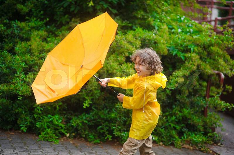 The fellow is dressed in a bright yellow raincoat. He likes to walk in the rain and the boy cheerfully laughs, stock photo