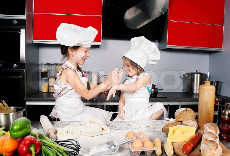 Two little girls having fun on the kitchen table with raw food, clothing cooks, stock photo