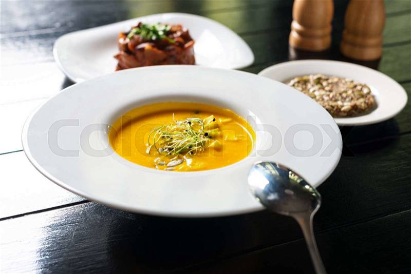 Vegan creamy pumpkin soup with crunchy cereal bread and cold salad of potatoes and green peas with carrots on the dinner table ready to eat, stock photo
