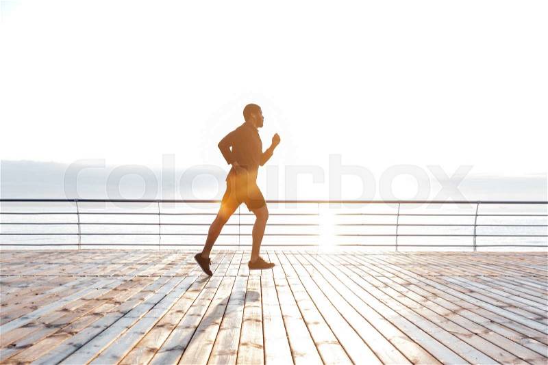 Attractive arfican young sportsman running running on pier at the sunset, stock photo