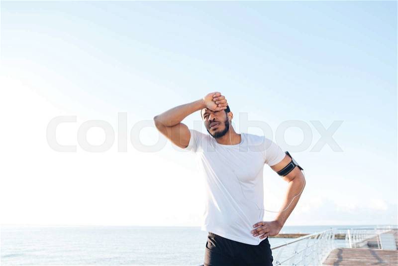 Portrait of exhausted african young sportsman tired after running standing outdoors, stock photo