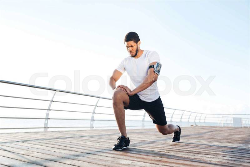 Sportsman warming up and stretching legs on pier, stock photo