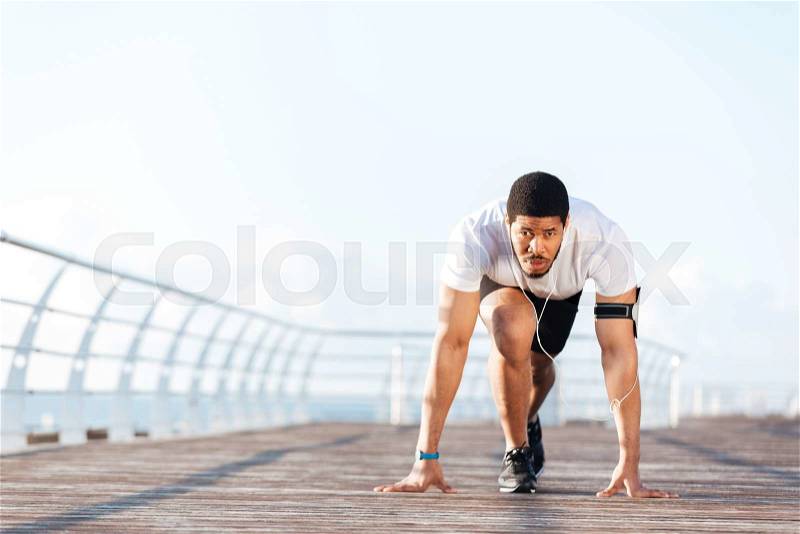 Focused sportsman in running start position on pier, stock photo