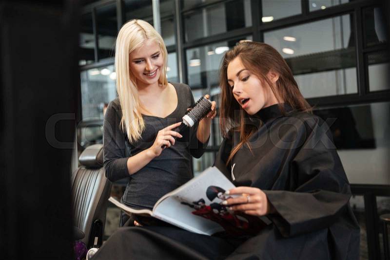 Young beautiful woman discussing hairstyling with her hairdresser while sitting in the hairdressing salon, stock photo