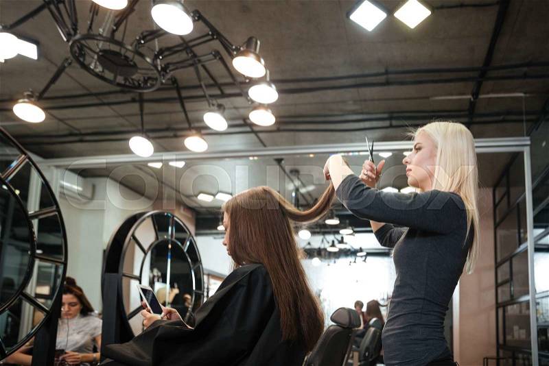 Young woman getting new haircut by female hairdresser at beauty salon, stock photo