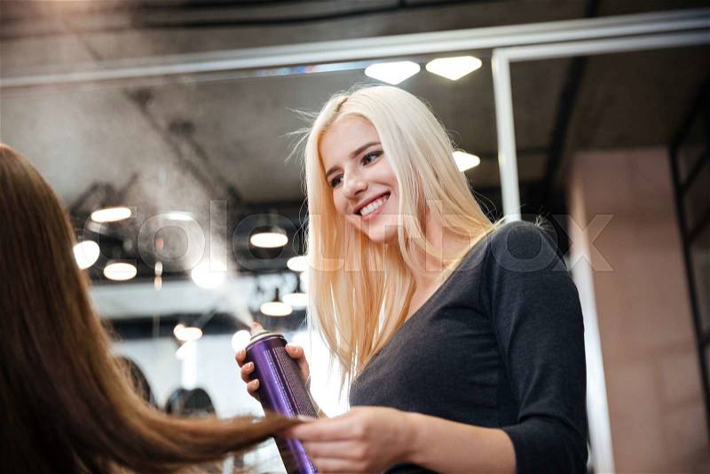 Close-up portrait of a hairdresser with hair spray fixating client hairdo at salon, stock photo