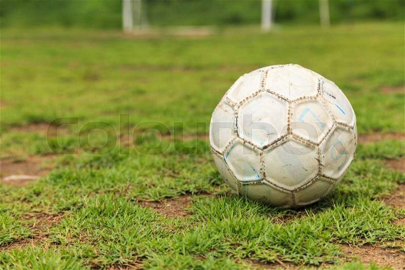 Old white soccer ball on the rough grass field, stock photo