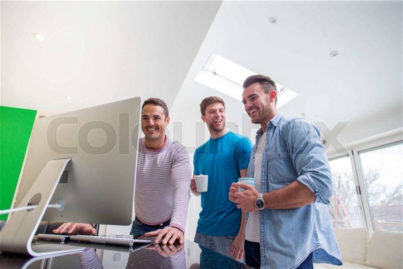 A small group of men are stood around a computer, they are all laughing and smiling looking at the computer, stock photo