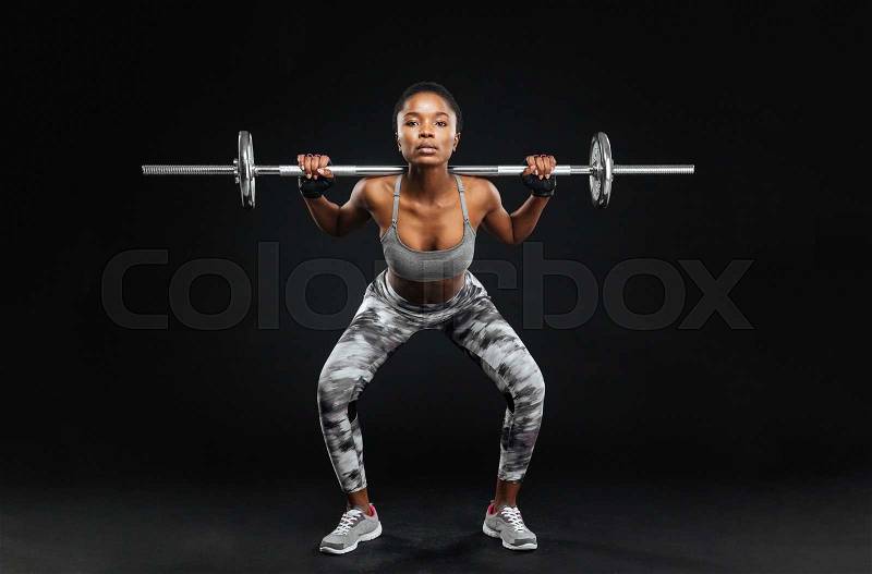 Close-up portrait of a fitness young girl doing squats with barbell at the gym isolated on a black background, stock photo
