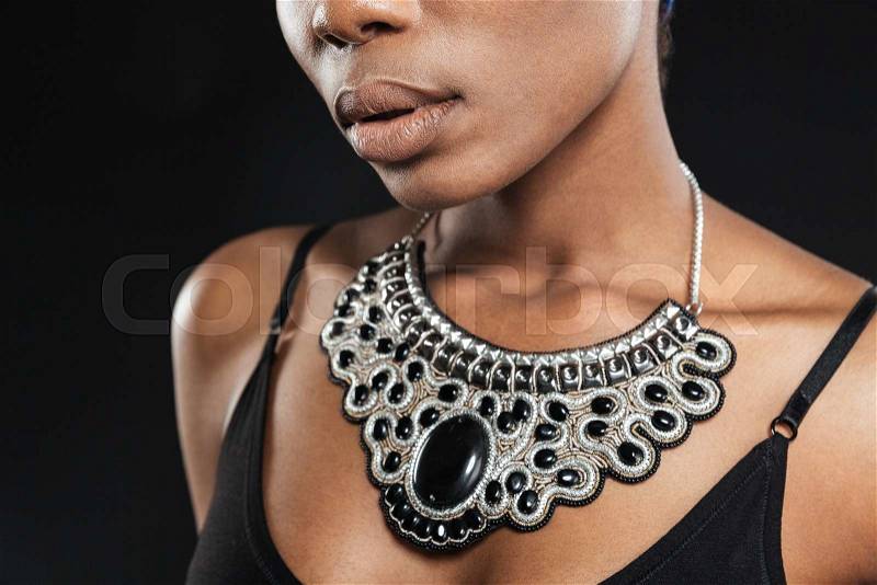 Cropped image of a beautiful african woman wearing necklace isolated on the black background, stock photo
