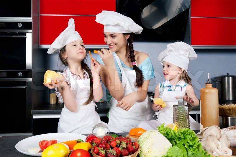 Mom teaches two daughters to cook at the kitchen table with raw food, clothing cooks, stock photo