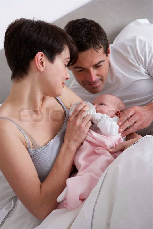 Parents Feeding Newborn Baby In Bed At Home, stock photo