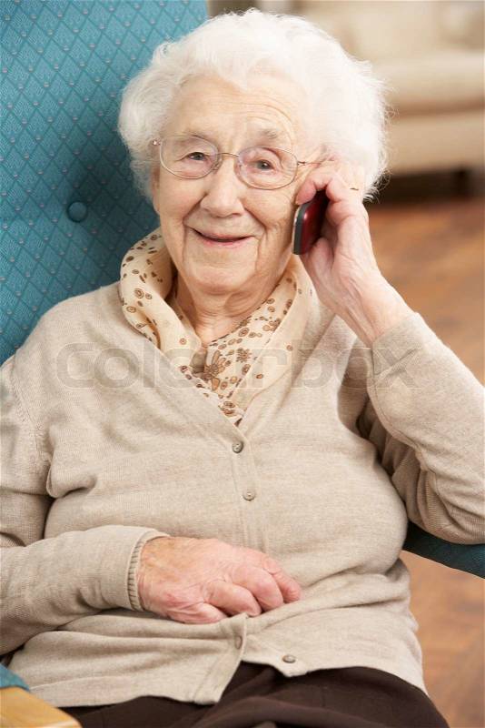 Senior Woman Talking On Mobile Phone Sitting In Chair At Home, stock photo