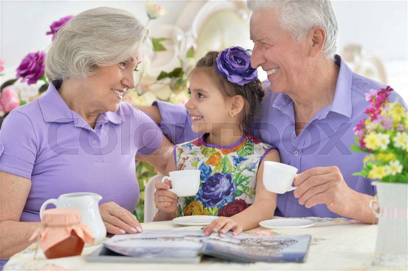 Grandparents with granddaughter drinking tea and reading magazine, stock photo