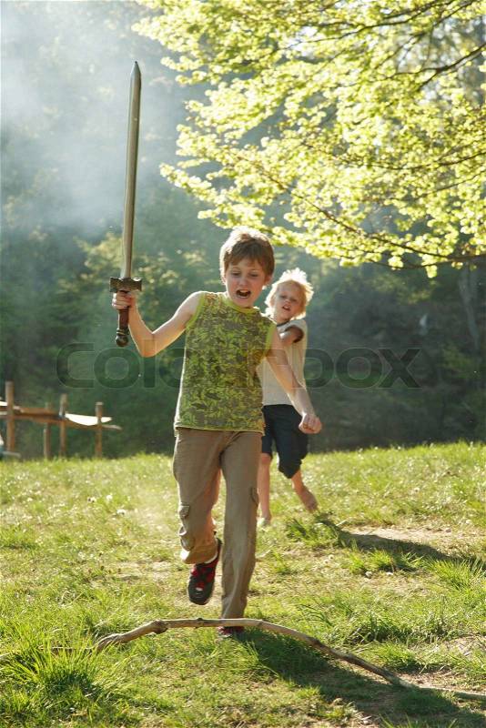 Two small boys playing whith rubber swords in the nature, one is chasing the other. The sun is shining, stock photo