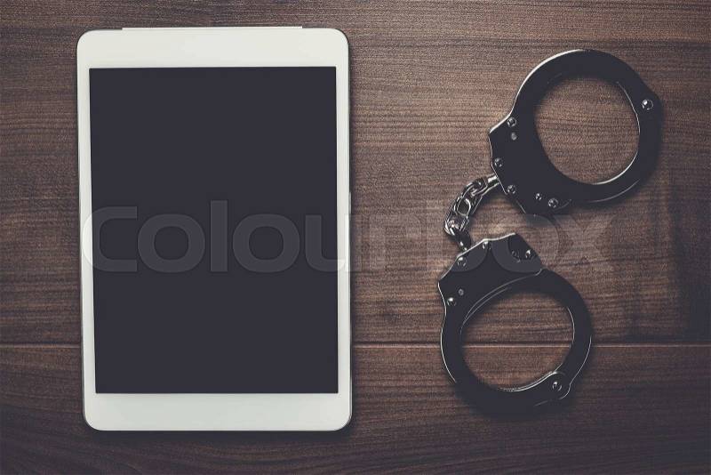 Handcuffs and tablet computer on brown wooden background, stock photo