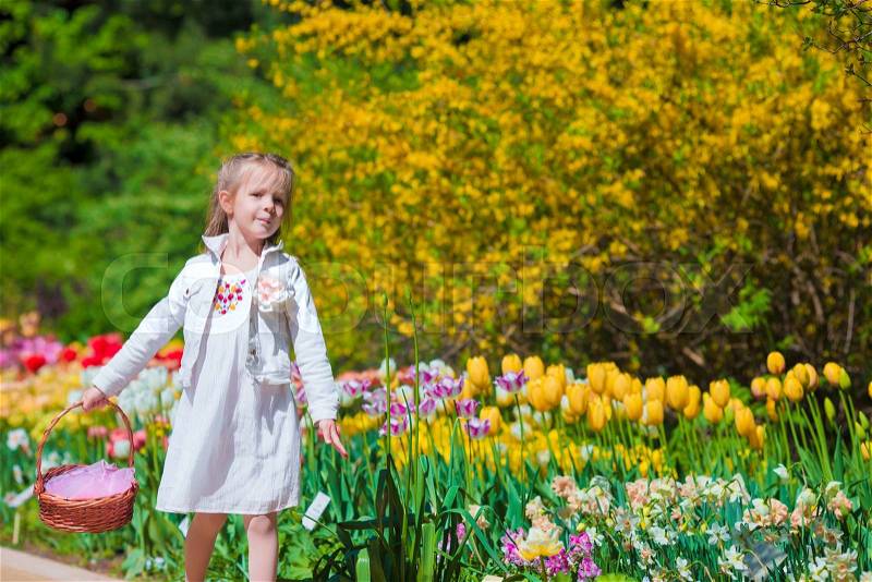 Spring garden, spring flowers, adorable little girl and tulips. Cute kid with a basket in blooming garden on warm day, stock photo