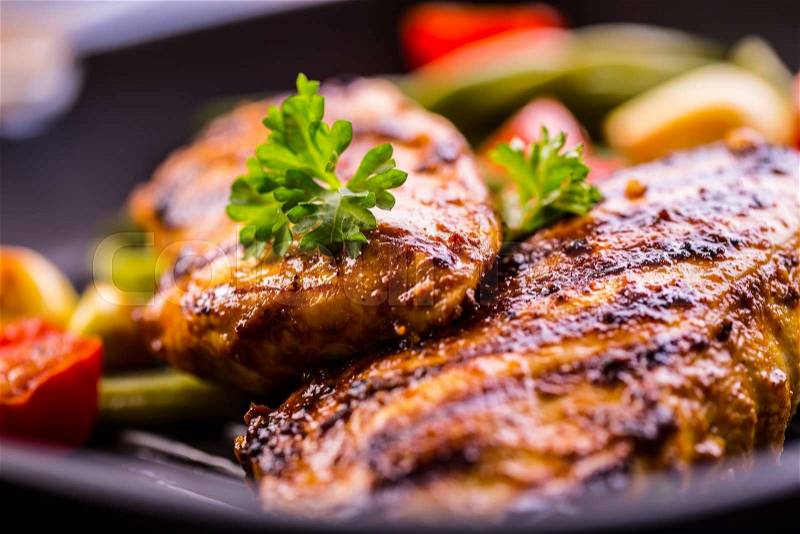 Grilled chicken breast in different variations with cherry tomatoes, green French beans, garlic, herbs, cut lemon on a wooden board or teflon pan. Traditional cuisine. Grill kitchen. , stock photo