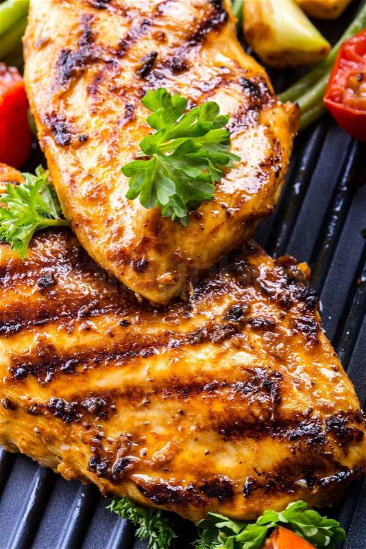 Grilled chicken breast in different variations with cherry tomatoes, green French beans, garlic, herbs, cut lemon on a wooden board or teflon pan. Traditional cuisine. Grill kitchen.\, stock photo