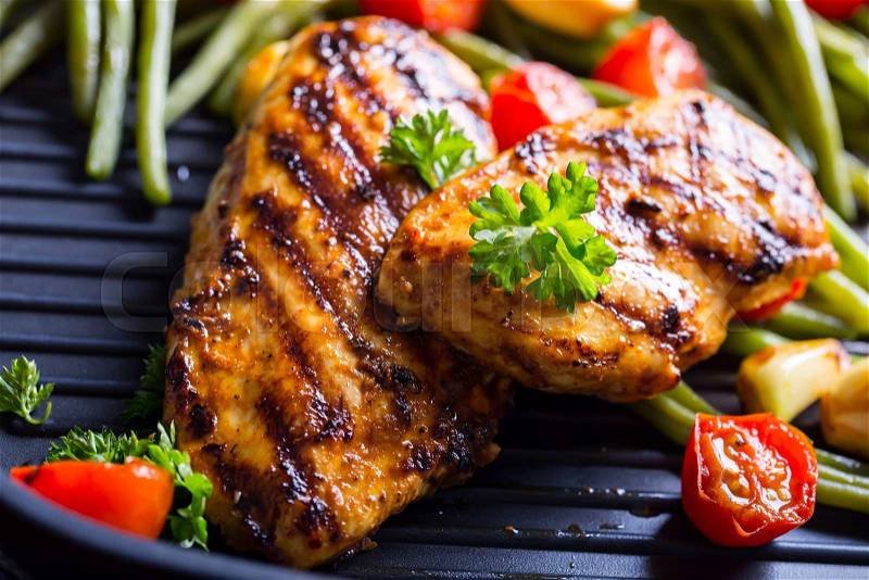 Grilled chicken breast in different variations with cherry tomatoes, green French beans, garlic, herbs, cut lemon on a wooden board or teflon pan. Traditional cuisine. Grill kitchen. , stock photo