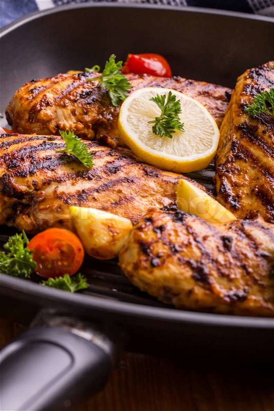 Grilled chicken breast in different variations with cherry tomatoes, green French beans, garlic, herbs, cut lemon on a wooden board or teflon pan. Traditional cuisine. Grill kitchen.\, stock photo