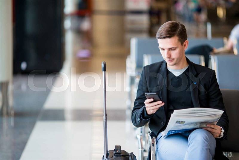 Passenger in an airport lounge waiting for flight aircraft. Young man with cellphone in airport waiting for landing, stock photo