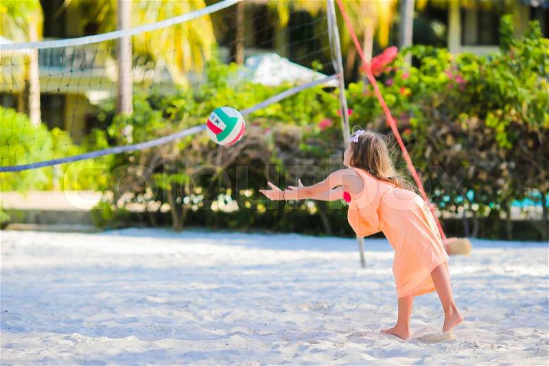 Little active girl playing voleyball on beach with ball. Sporty flid enjoying beach game outdoors, stock photo