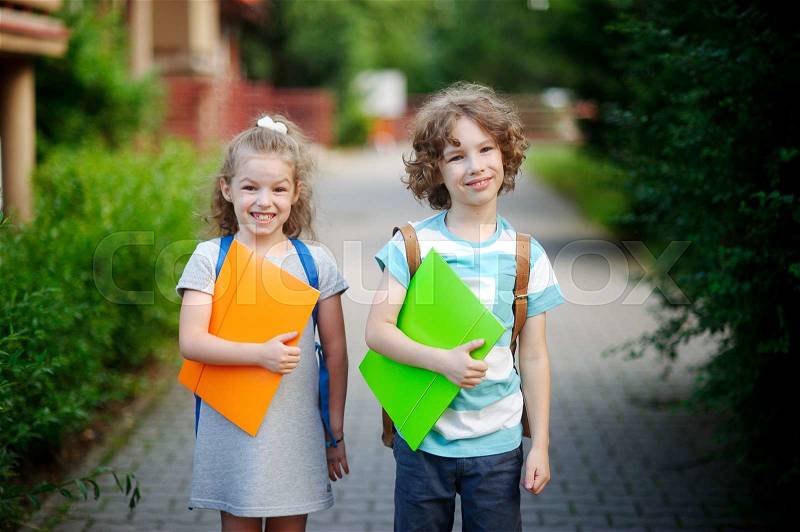 Boy and gerl on the way to school. Two pupils of elementary school. Behind the back of everyone a satchel, in hands - the bright folder. Children smile, stock photo