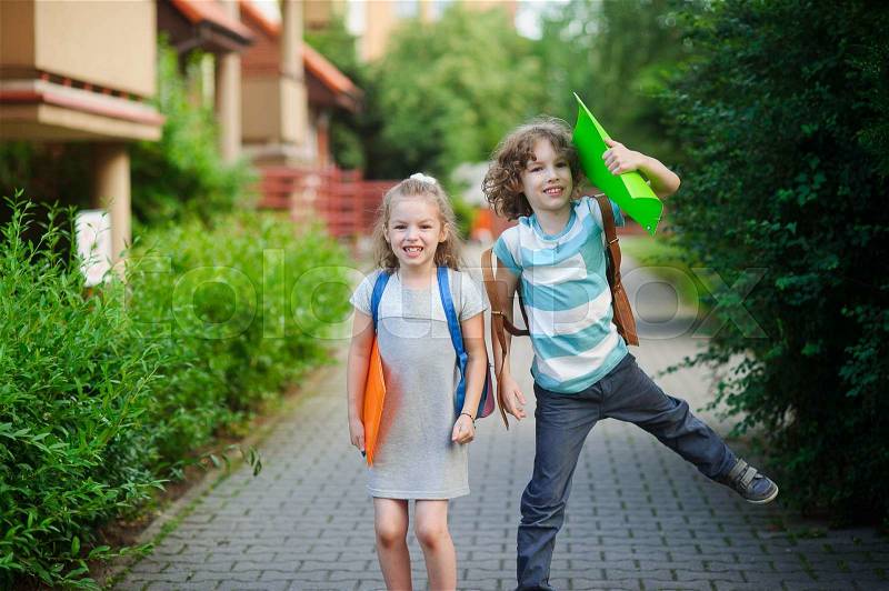 Two children have fun on the way to school. Boy and girl pupils of elementary school. Behind the back of them school bags. Children laugh looking in the camera, stock photo