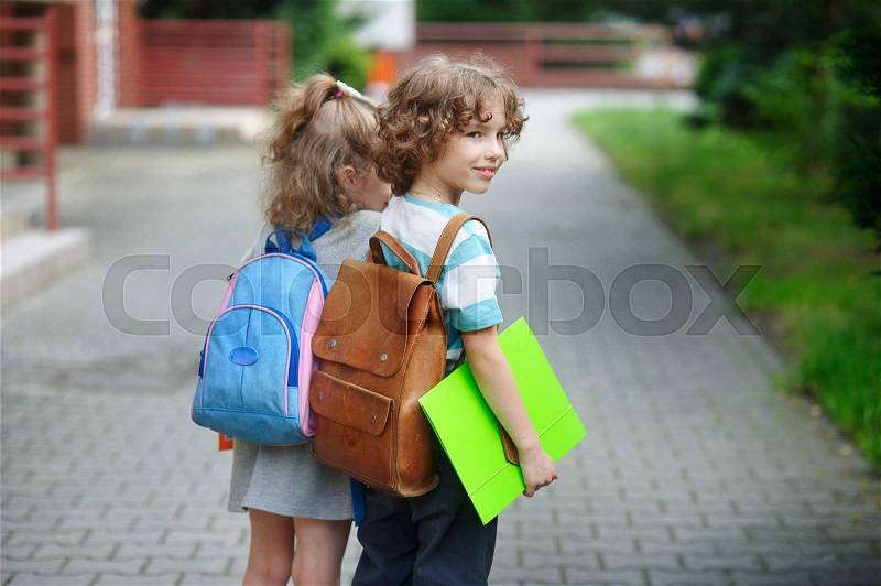 Two little pupil of elementary school, boy and girl, stand having joined hands. The boy with a smile looks somewhere. It costs in a half-turn to the camera, stock photo