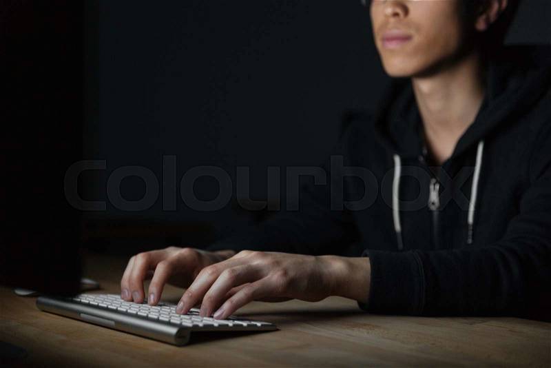 Closeup of serious asian young man sitting and typing on keyboard in dark room, stock photo