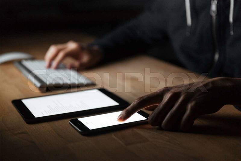 Closeup of young man using blank screen and cell phone on the table, stock photo