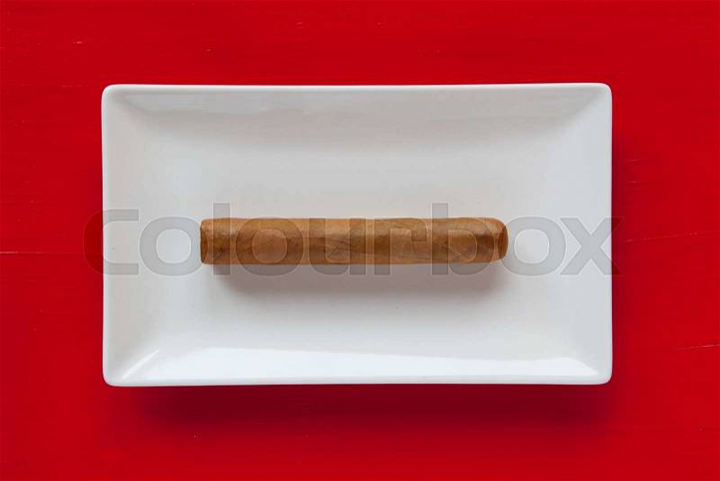 White ceramic dish with luxury Cuban cigar on over red background, rectangle dish, stock photo