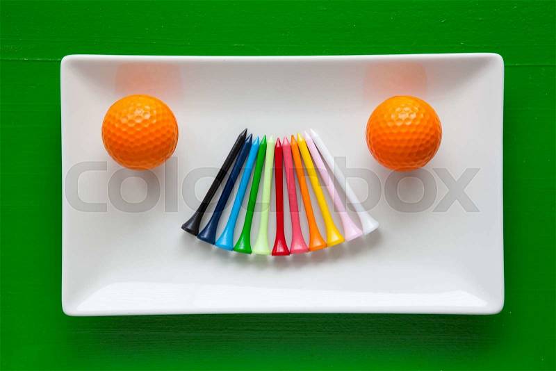 White ceramic dishes with golf wooden tees and white balls on over green background, rectangle dish, stock photo