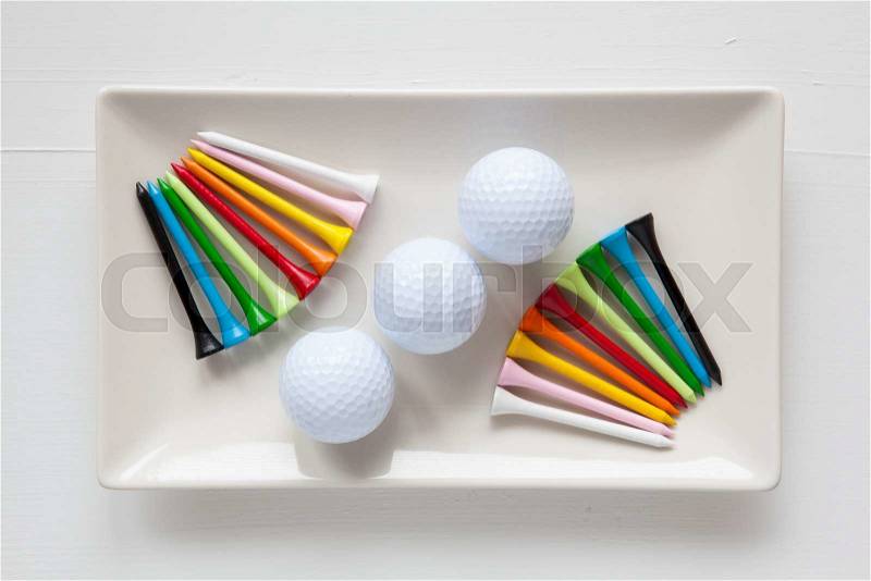 White ceramic dishes with golf balls and wooden tees on over white background, rectangle dish, stock photo