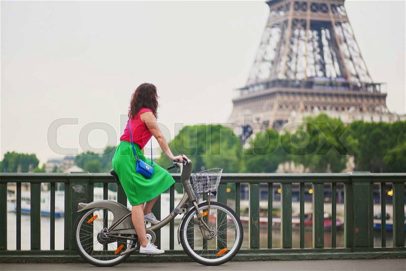 Beautiful young woman in green dress riding a bicycle on a street of Paris, near the Eiffel tower, stock photo