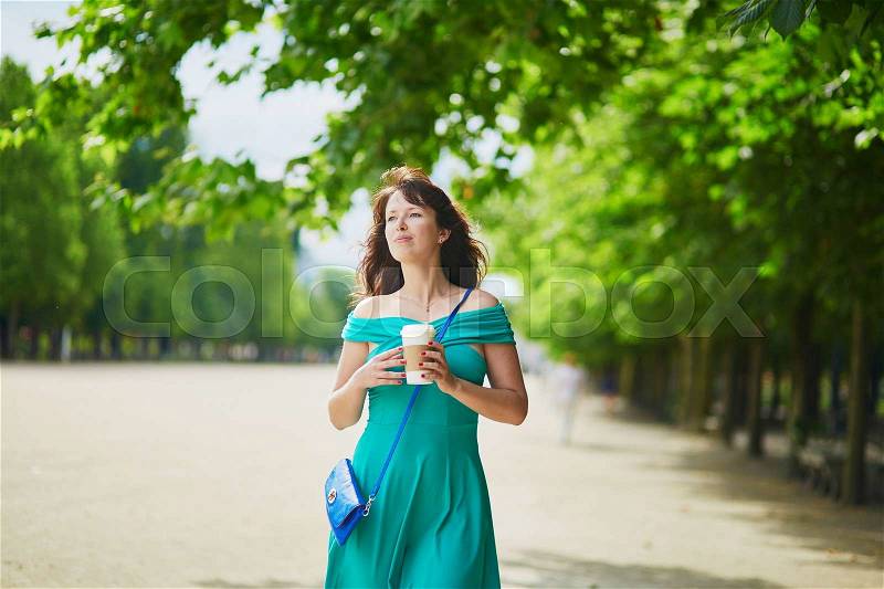 Beautiful young woman in green dress walking with coffee to go in Tuileries garden of Paris, France, stock photo