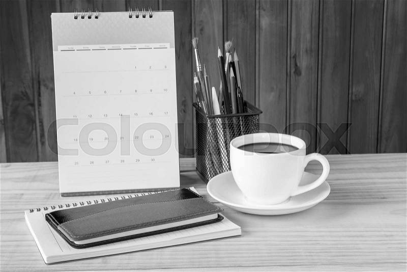 Black and white note book,coffee cup,and stack of book with calendar on wooden table background. Business concept, stock photo