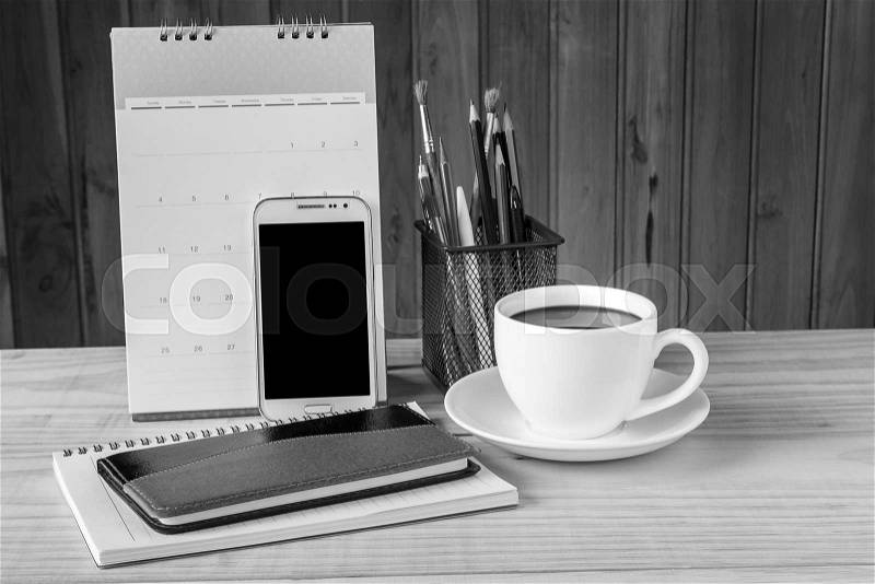 Note book,smart phone,coffee cup,and stack of book with calendar on wooden table background. Black and white tone, stock photo