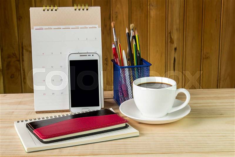 Note book,smart phone,coffee cup,and stack of book with calendar on wooden table background, stock photo
